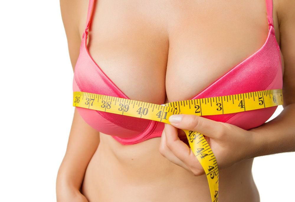 A woman in a pink bra measuring her breasts